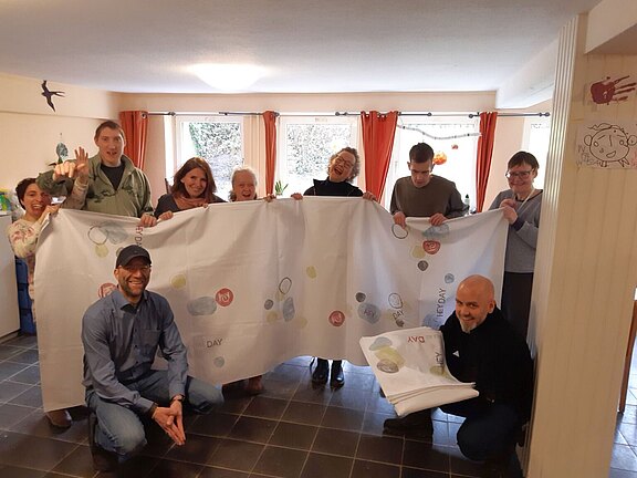 Foto: Die Mitglieder der Kunstgruppe der Stiftung Waldheim präsentieren eine von ihnen verzierte Tischdecke.